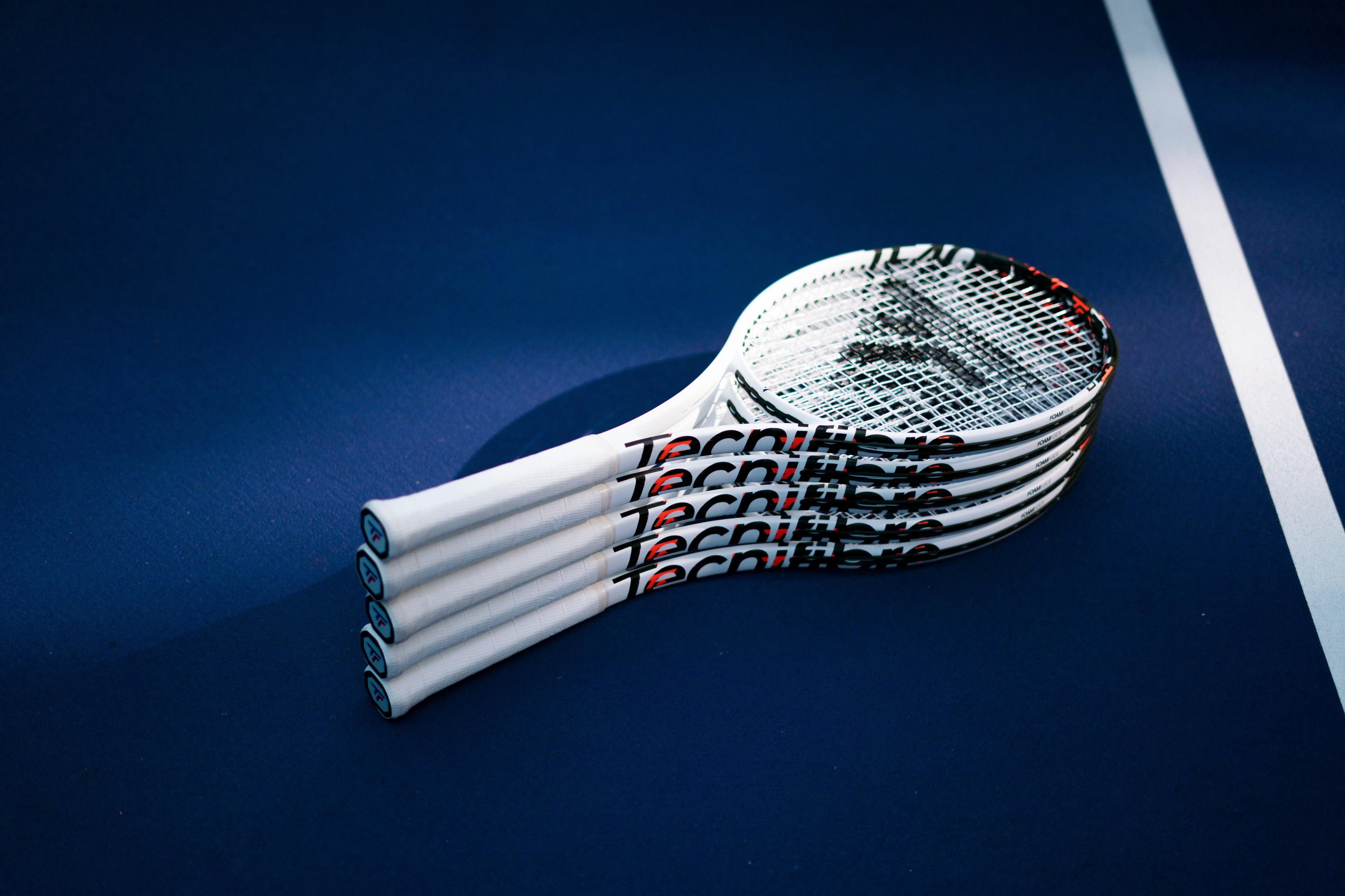 Stack of white Tecnifibre TF40 305 tennis racquets with black and red accents on a blue court.