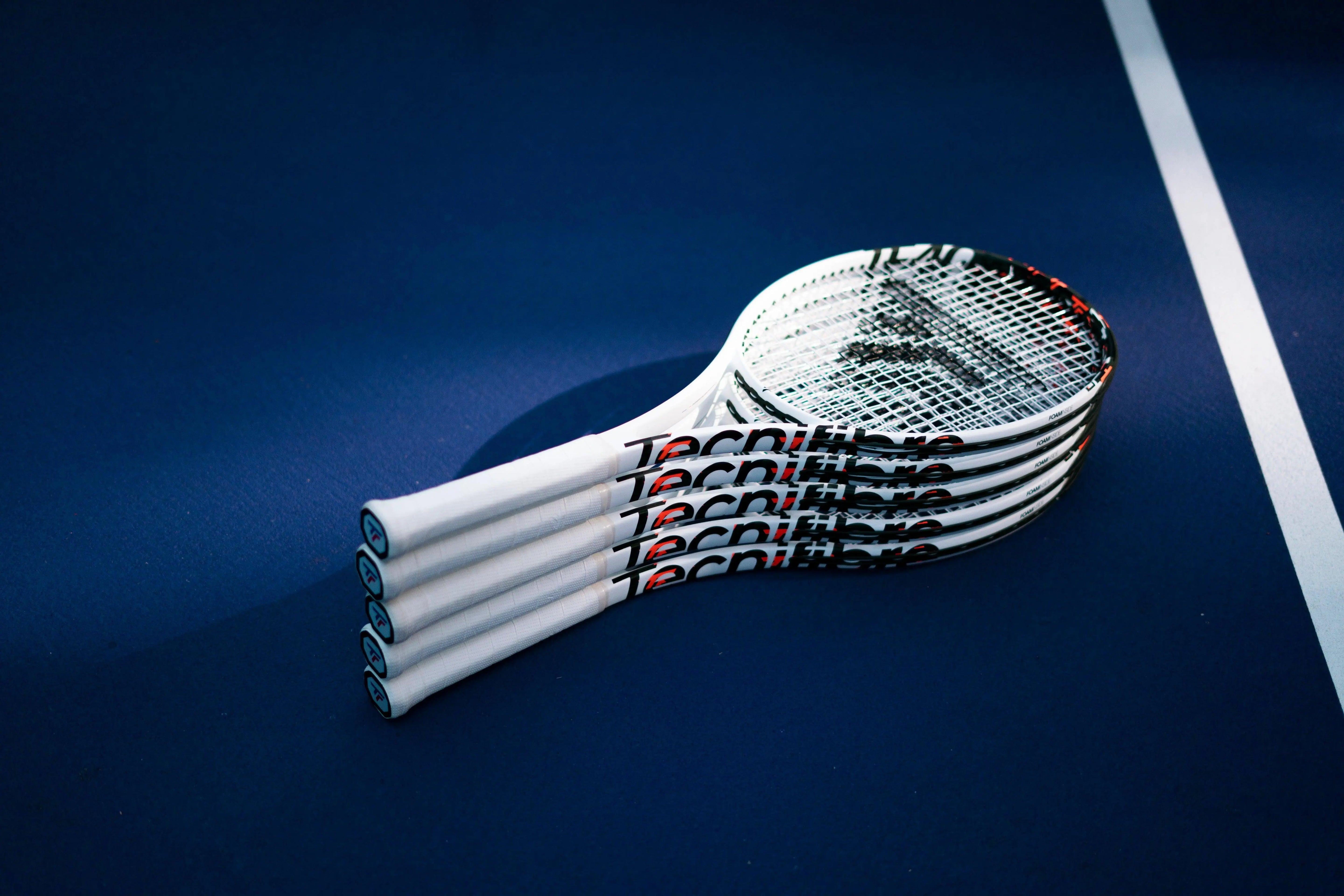 Stack of white Tecnifibre TF40 305 tennis racquets with black and red accents on a blue court.