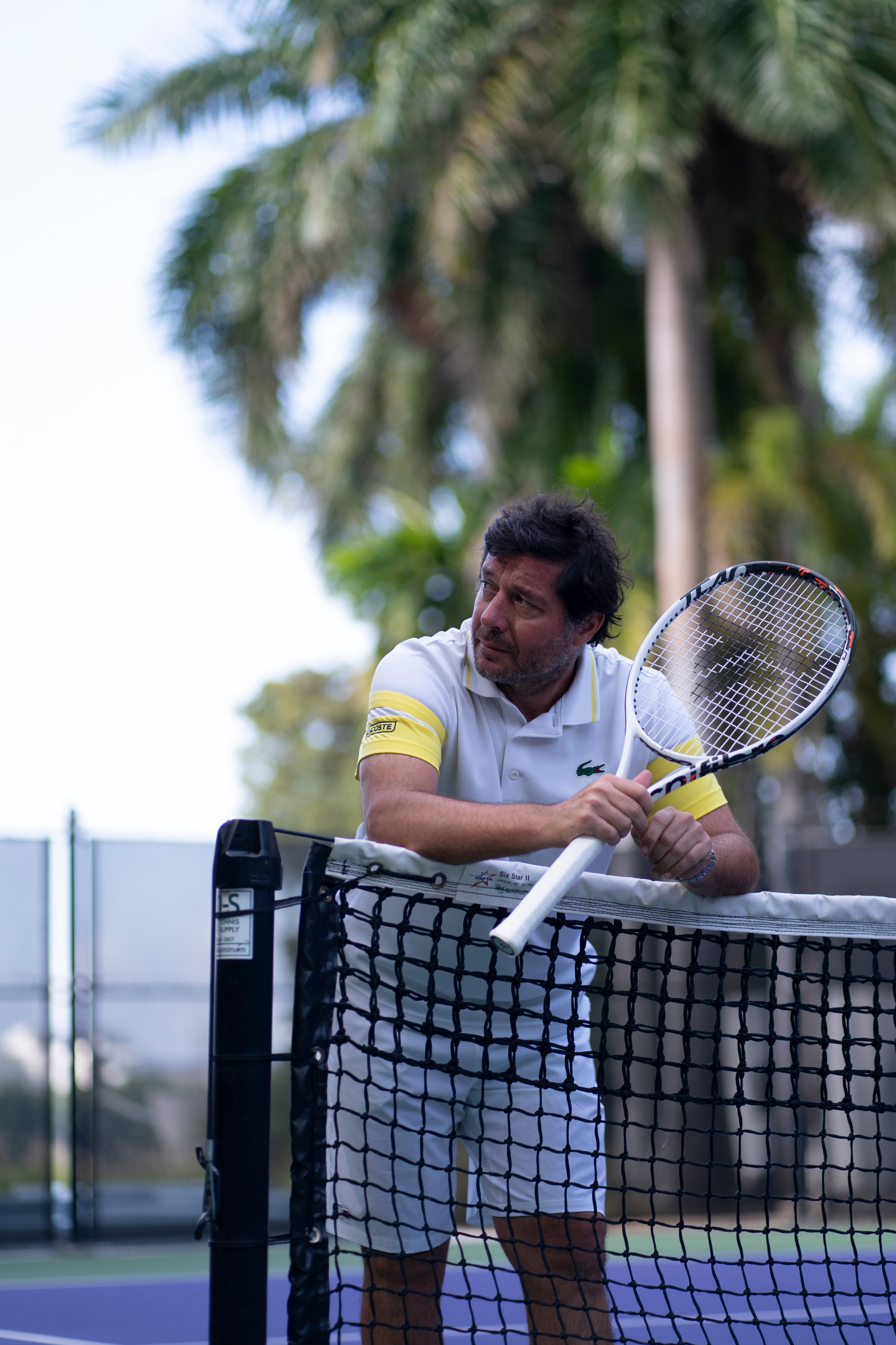 Man in white polo with yellow sleeves holding a white Tecnifibre TF40 305 tennis racquet on court.
