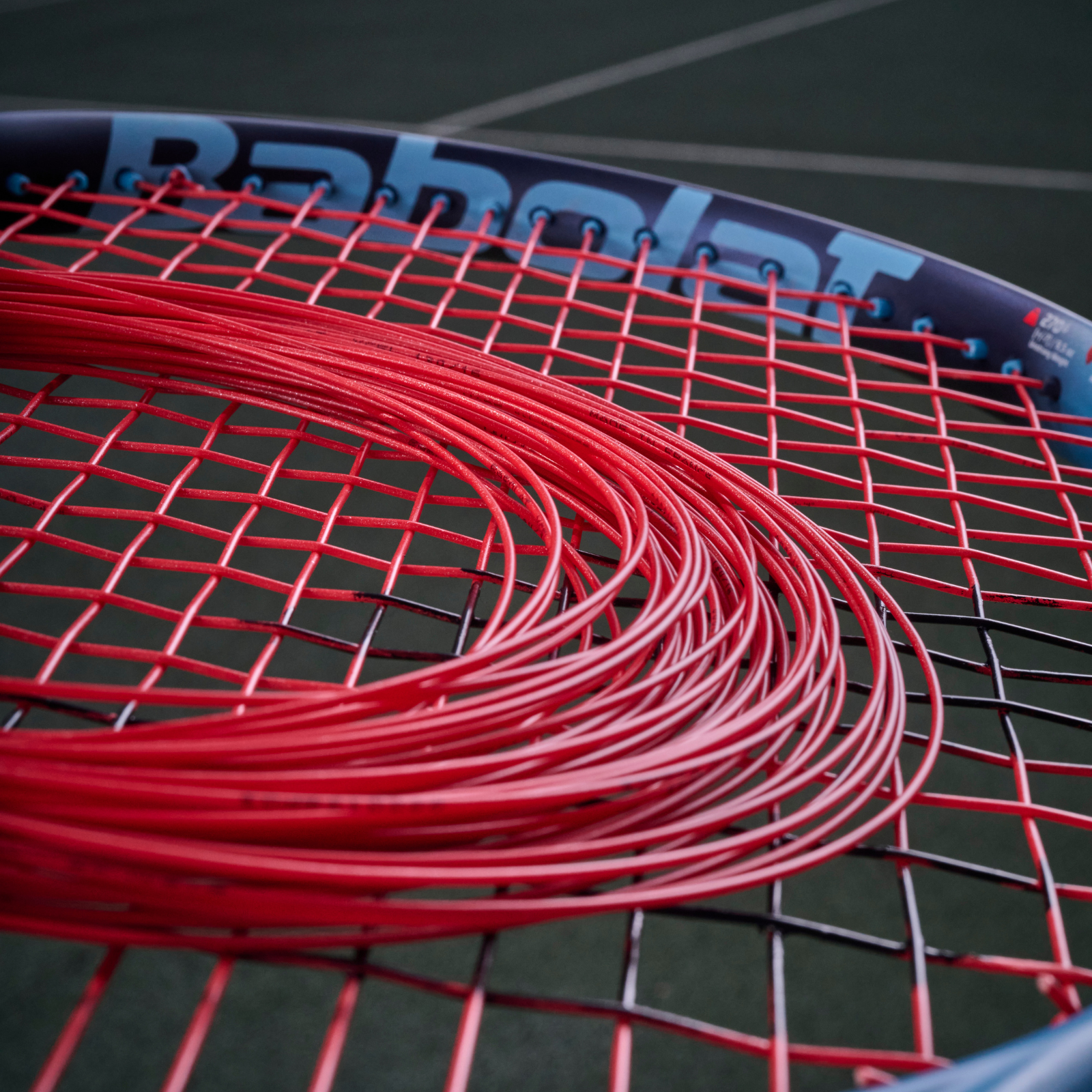 Coiled red Babolat XCEL 1.25mm multifilament tennis string on a racket's red and black string bed.