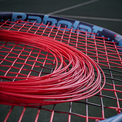 Coiled red Babolat XCEL 1.25mm multifilament tennis string on a racket's red and black string bed.