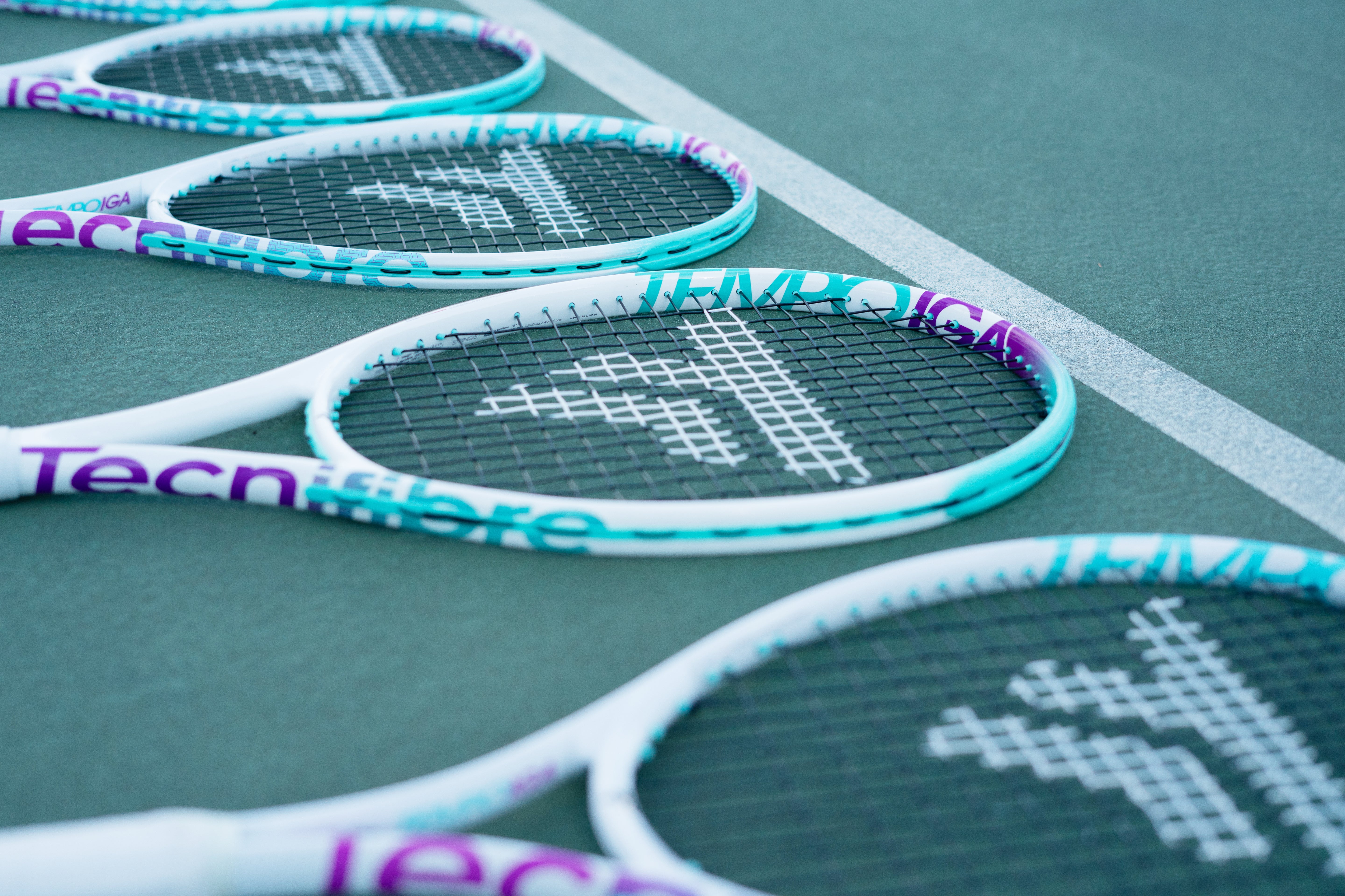 White Tecnifibre Tempo Iga 24 junior tennis racquets with turquoise and purple accents on a green court.