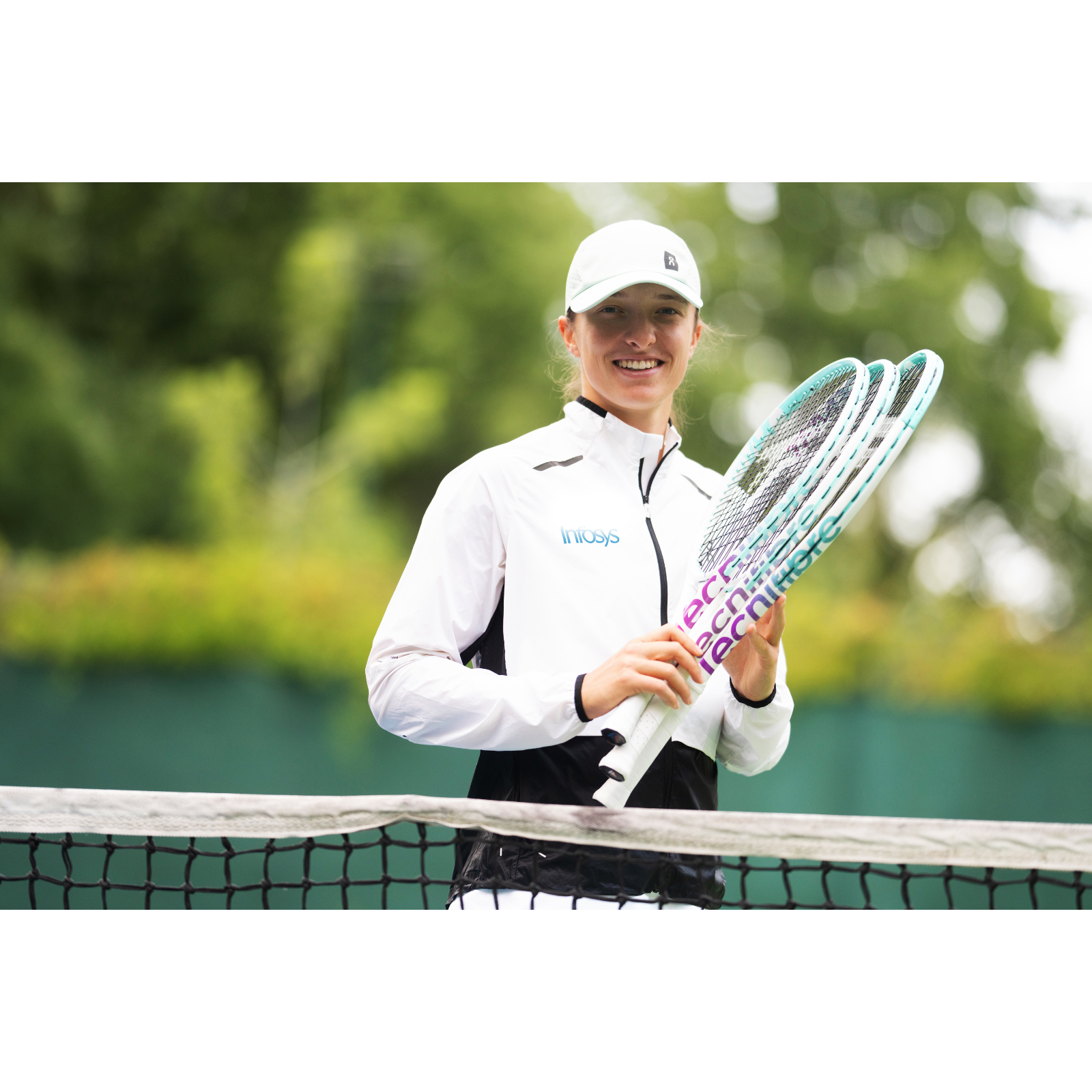 Iga Świątek holding two Tecnifibre Junior Tempo Iga 24 tennis racquets with white, purple, and teal accents.