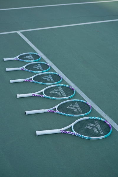 Six Tecnifibre Tempo Iga 26 junior tennis racquets with white, teal, and purple accents on a green court.