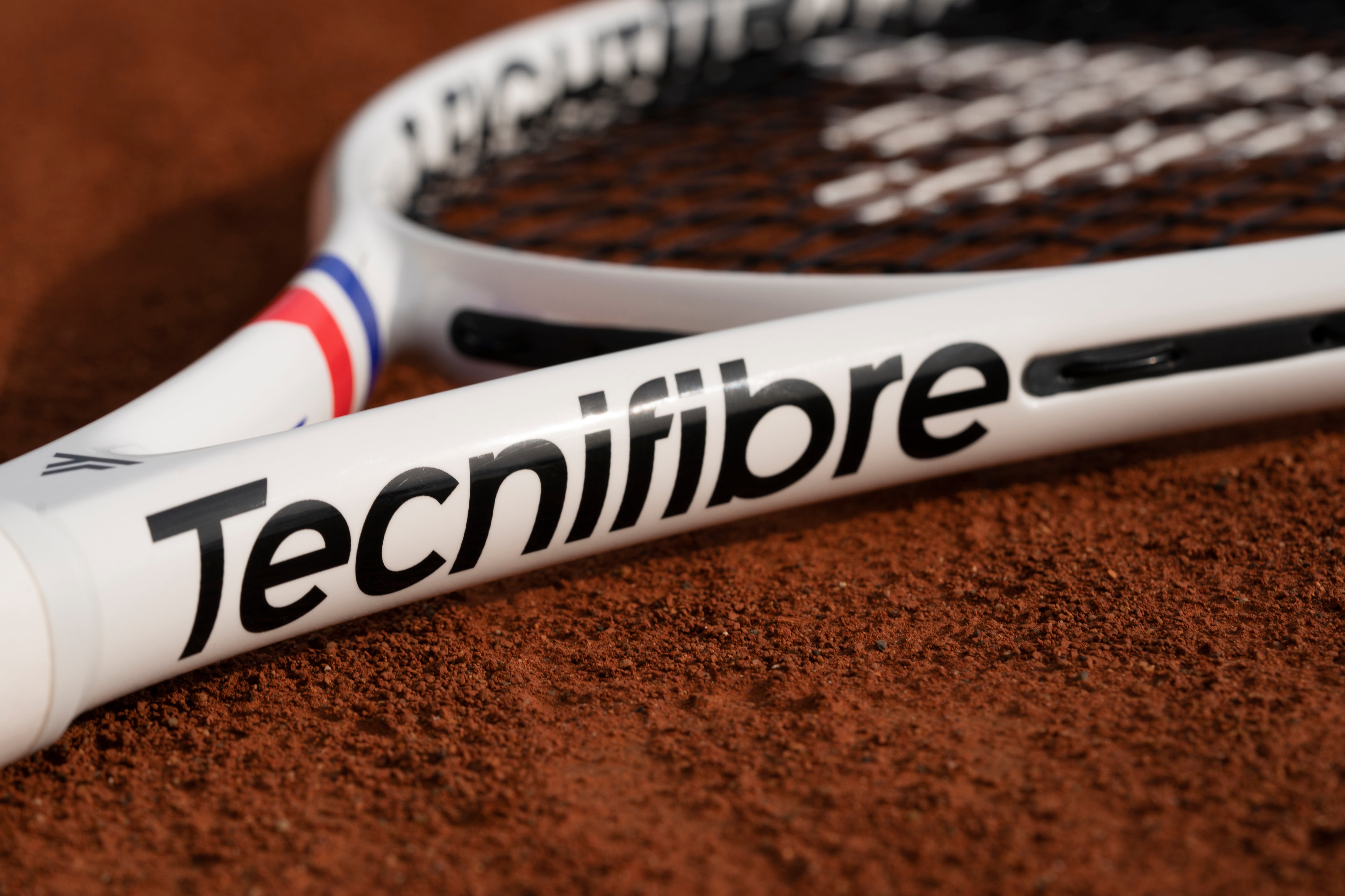 White Tecnifibre TFight Team L tennis racquet with black logo, red and blue accents, on a clay court.