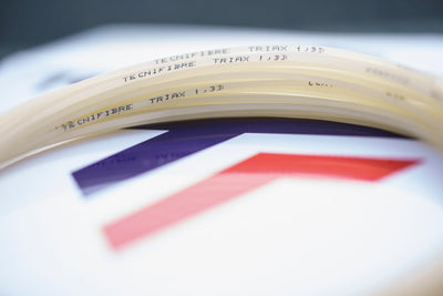 Coiled natural Tecnifibre Triax 1.33 tennis string with "Tecnifibre Triax 1.33" printed on it.