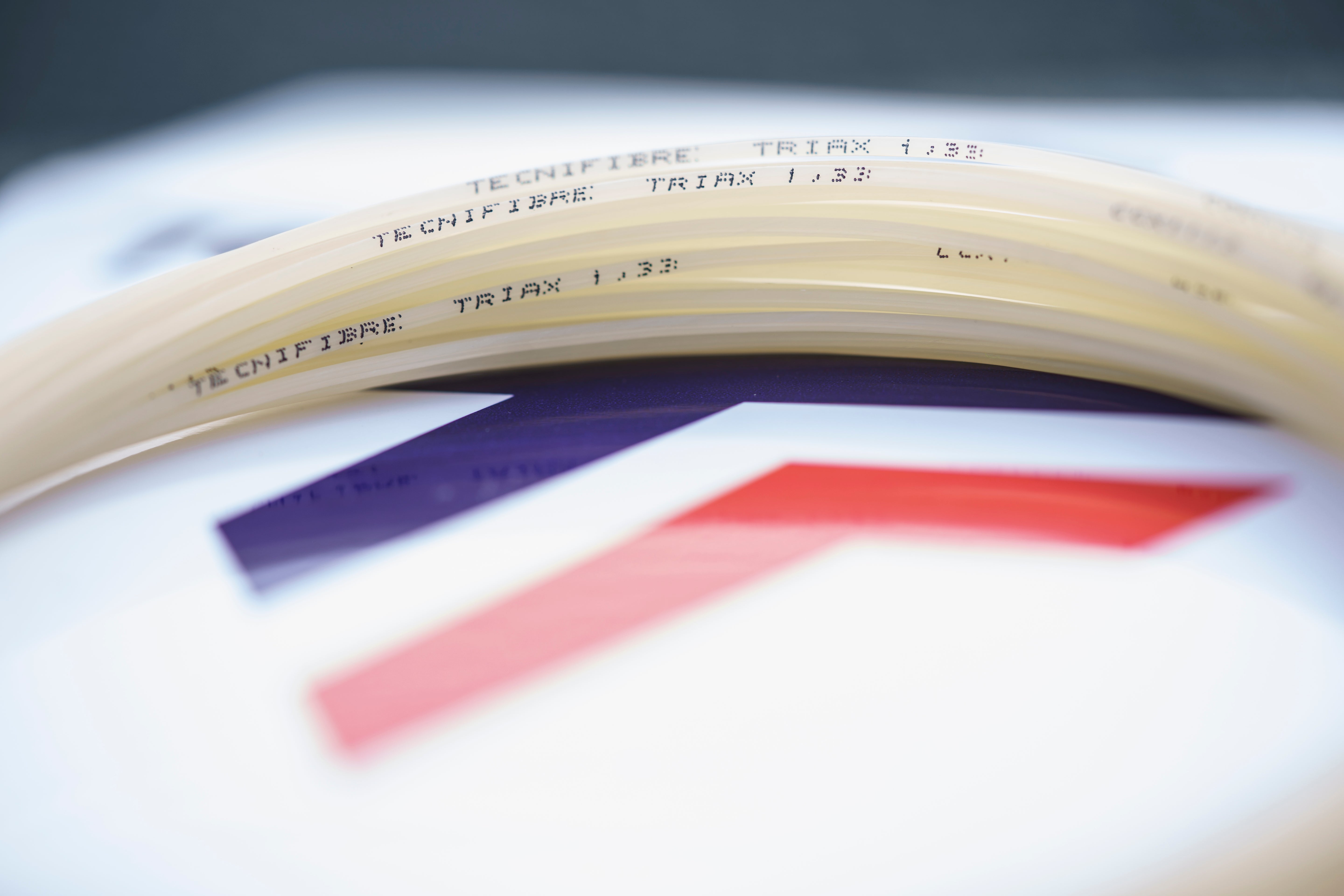 Coiled natural Tecnifibre Triax 1.33 tennis string with "Tecnifibre Triax 1.33" printed on it.