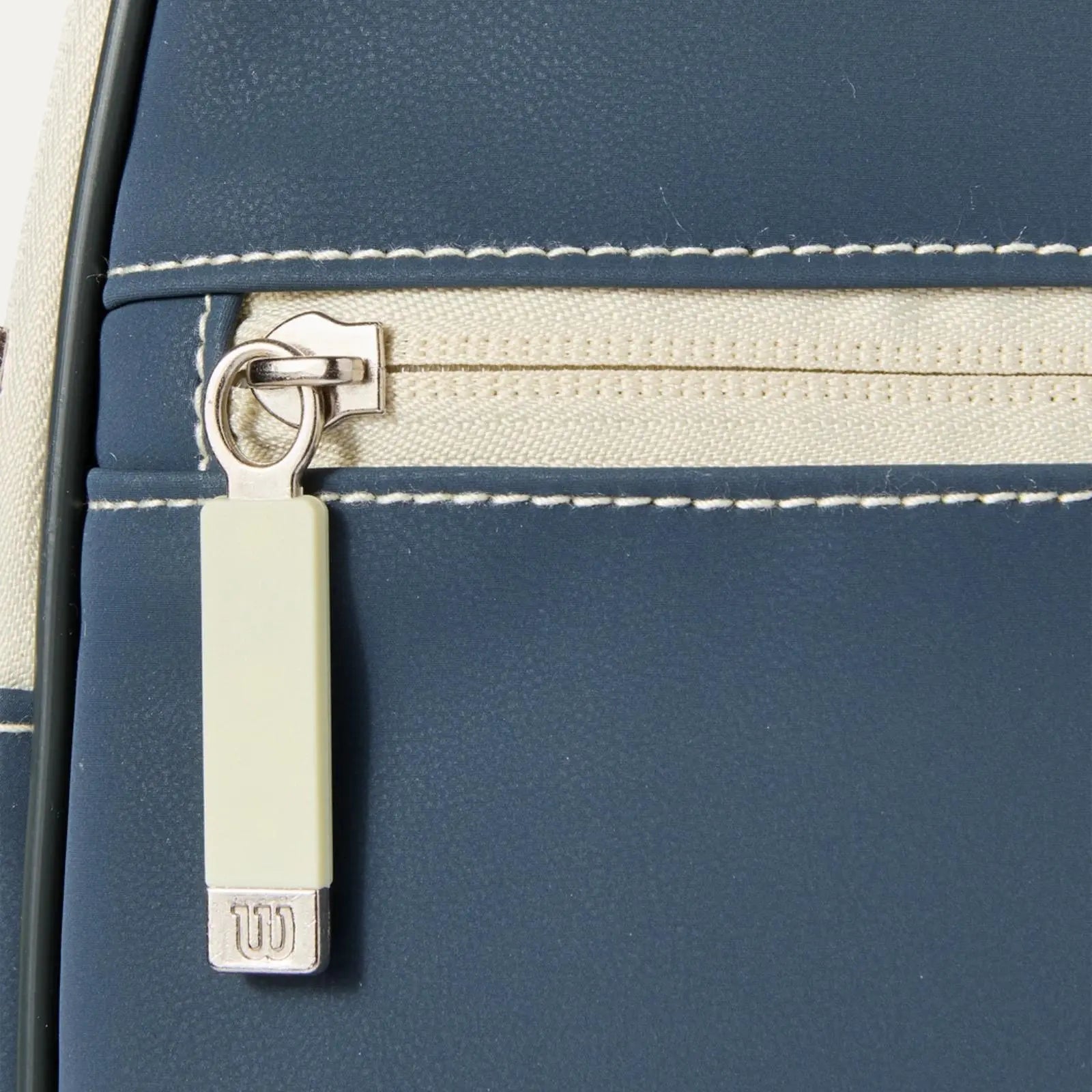 Close-up of a navy blue Wilson pickleball paddle cover with a cream zipper and white stitching.