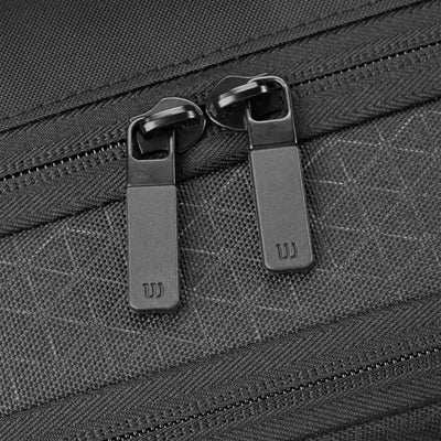 Close-up of a black Wilson tennis bag with two black zipper pulls featuring the "W" logo and a subtle triangle pattern.