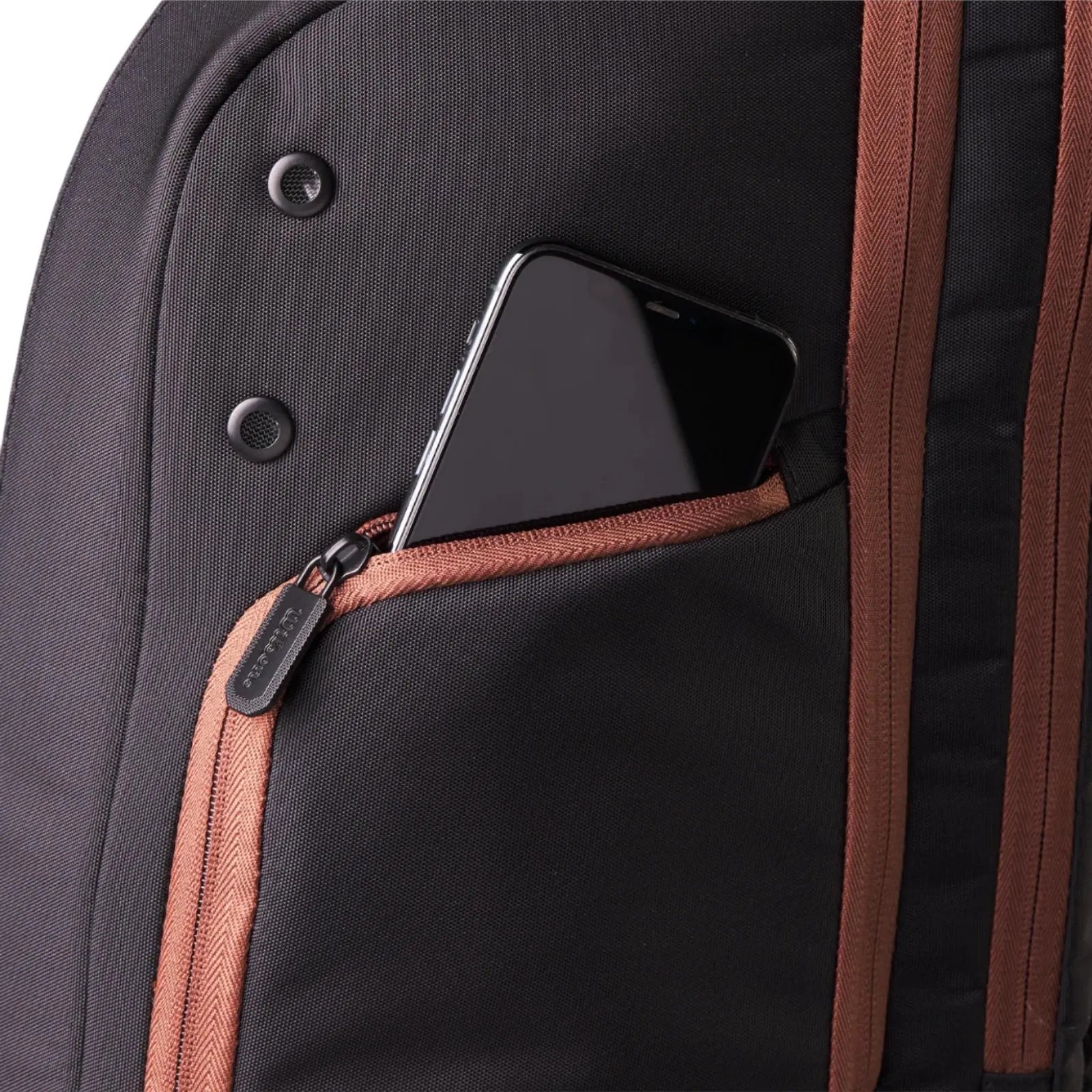 Close-up of a black Wilson Super Tour Pro Staff tennis backpack with a gold-brown zippered accessory pocket holding a smartphone.