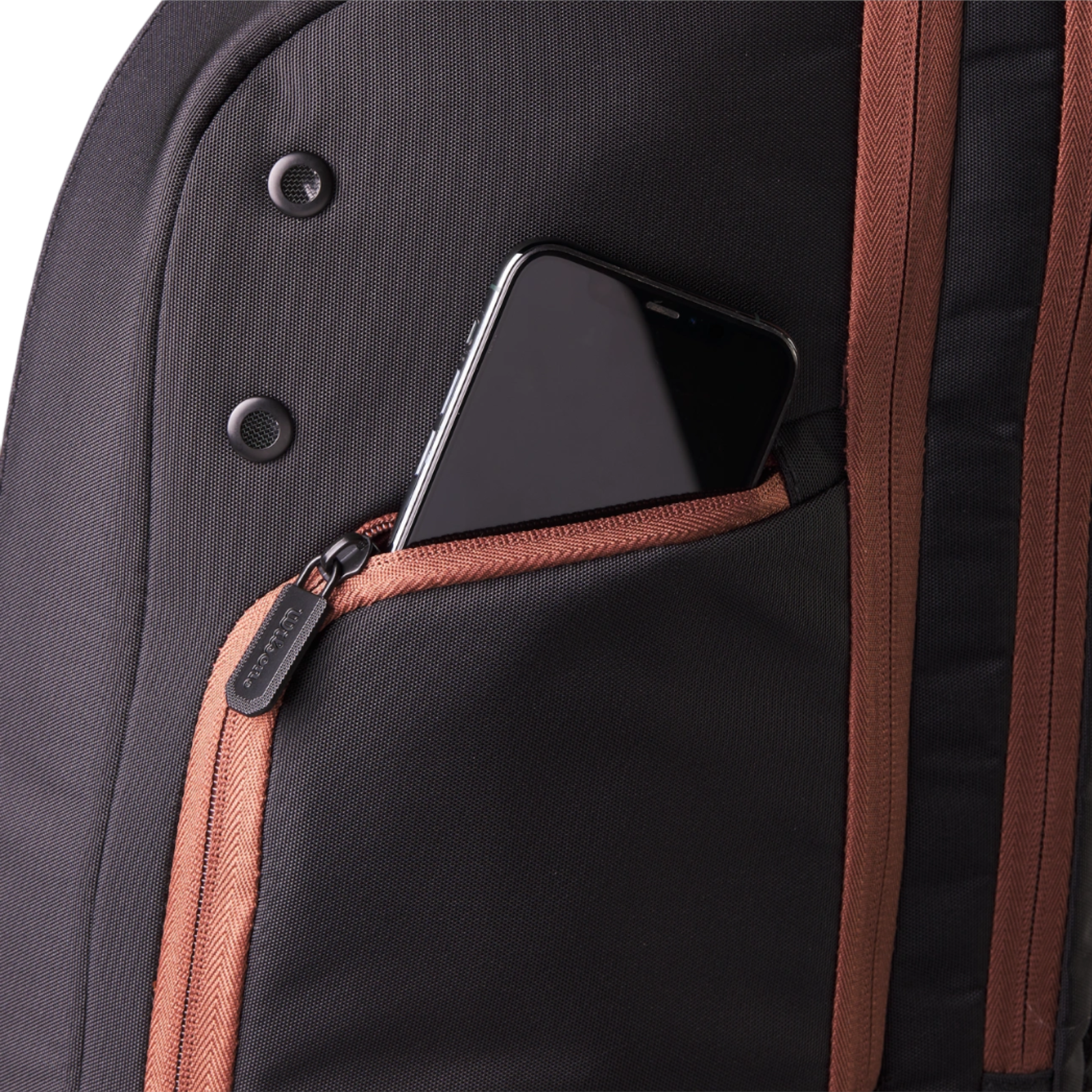 Close-up of a black Wilson Super Tour Pro Staff tennis backpack with a gold-brown zippered accessory pocket holding a smartphone.