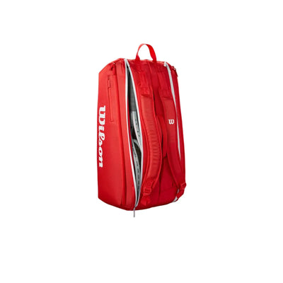 Red Wilson Super Tour tennis bag with white logos, padded backpack straps, and a partially unzipped main compartment.