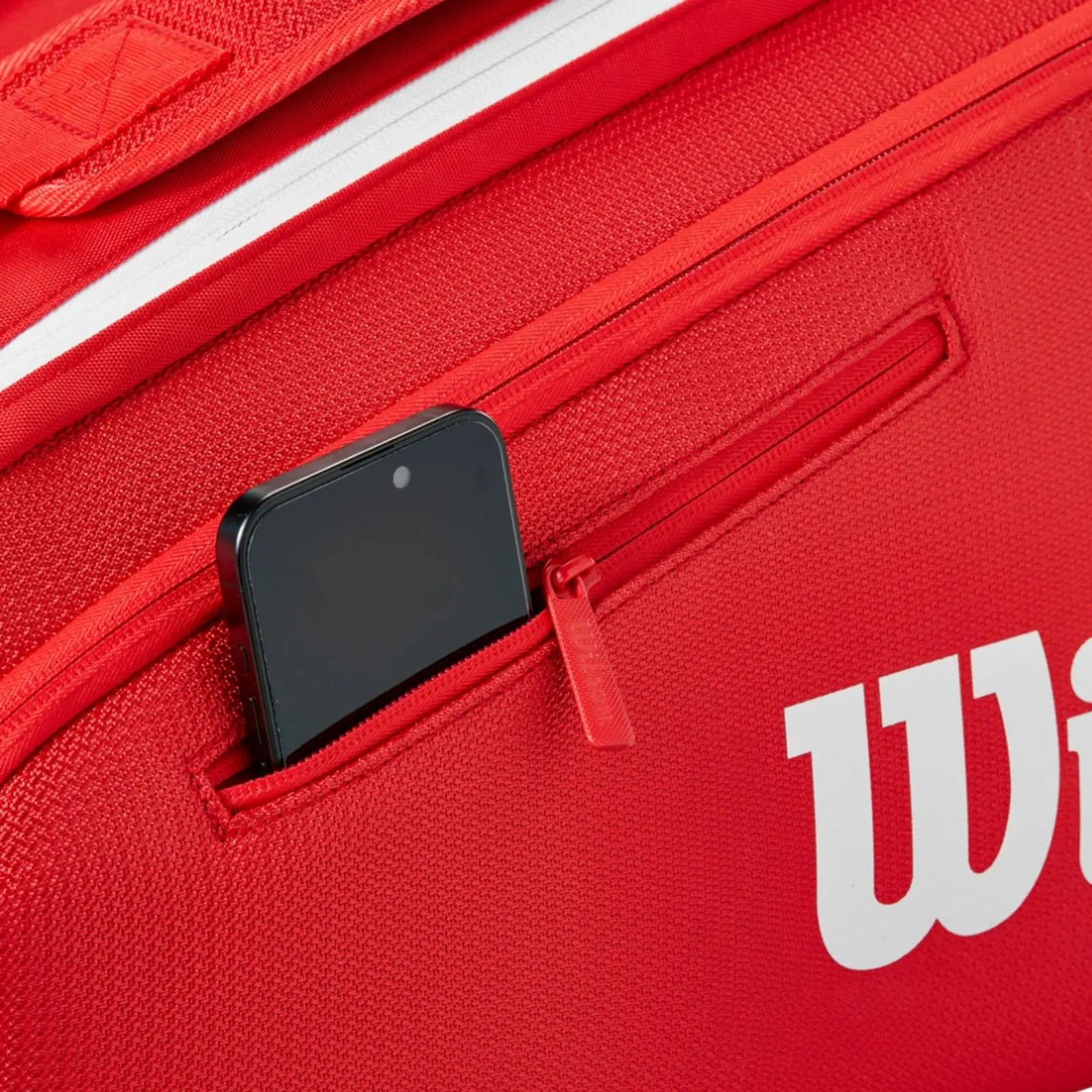 Close-up of a red Wilson Super Tour tennis bag with a black smartphone in a zippered exterior pocket.