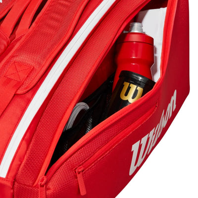 Red Wilson Super Tour tennis bag with a zippered compartment holding a red water bottle and black accessories.