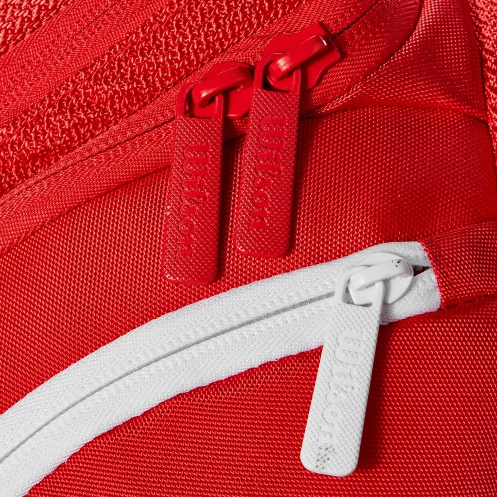 Close-up of a red Wilson Super Tour tennis backpack with red and white zippers.
