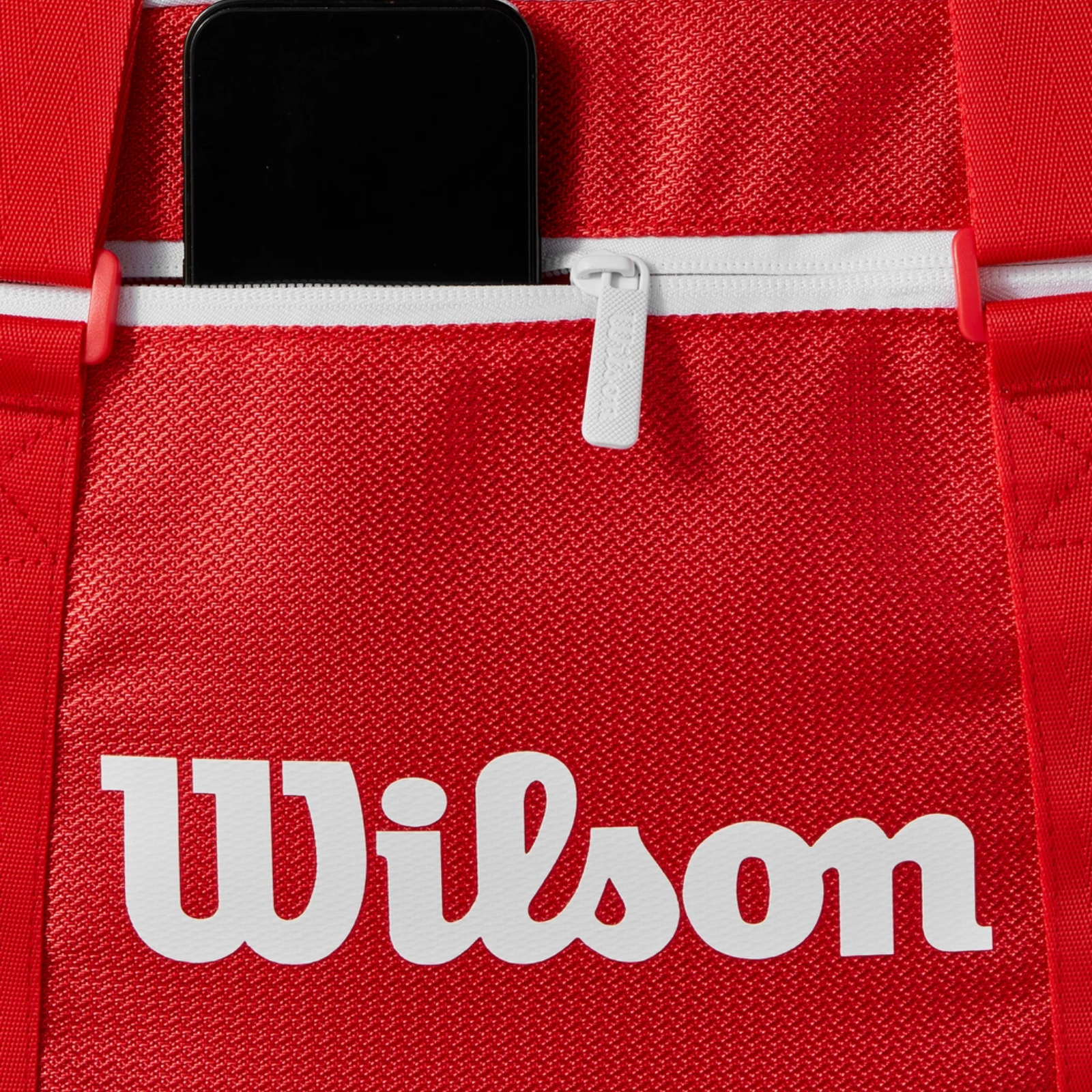 Red Wilson Super Tour small duffel bag with white logo, zipper, and phone in an accessory pocket.