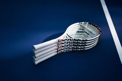 Stack of white Tecnifibre TF40 305 tennis racquets with black and red accents on a blue court.
